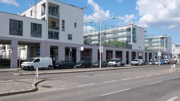 Moderne Wohn- und Geschäftsgebäude entlang einer Straße mit geparkten Autos unter blauem Himmel.