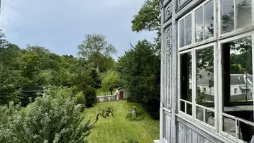 Blick aus einem historischen Fenster auf den weitläufigen Garten und die umliegende grüne Landschaft.