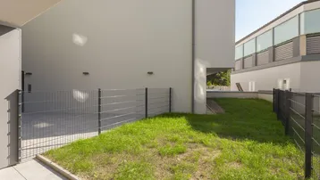 Kleine Rasenfläche und gepflasterte Terrasse neben einem modernen Gebäude mit klaren Linien.