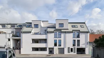 Moderne Wohnanlage mit weißer Fassade, Satteldach und integrierter Tiefgarage an der Straße.