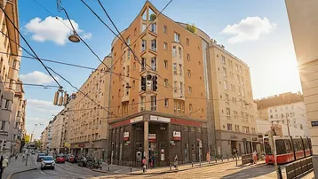 Gebäude an einer belebten Straßenecke mit moderner Architektur und Straßenbahnverkehr.