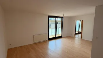 Helles Wohnzimmer mit Parkettboden, Heizkörper und Zugang zu einem Balkon.