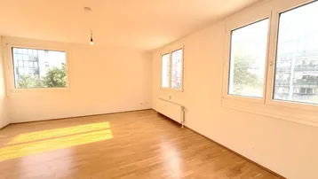Helles Wohnzimmer mit Parkettboden und mehreren Fenstern, das viel Tageslicht hereinlässt.