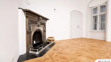 Heller Raum mit kunstvollem Parkettboden und einem eleganten, verzierten Kamin als Blickfang.