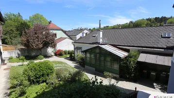 Malerischer Gartenbereich mit einem charmanten Wintergarten und üppiger Vegetation unter blauem Himmel.
