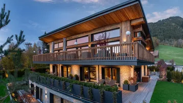 Moderne Holzfassade eines Chalets mit mehreren Balkonen und Bergblick bei Sonnenuntergang.