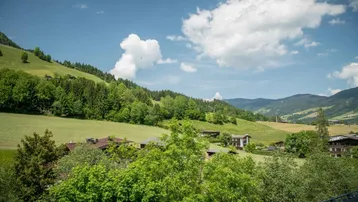 Weitläufiger Blick über die grüne, hügelige Landschaft mit vereinzelten Häusern unter blauem Himmel.