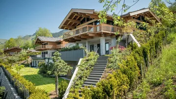 Modernes Chalet mit Holzfassade, Terrassen und gepflegter Gartenanlage am Hang.