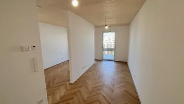 Lichtdurchfluteter Raum mit Fischgrätparkett, Holzdecke und Zugang zum Balkon.