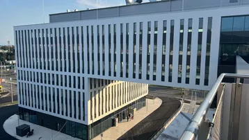 Modernes Bürogebäude mit markanter Architektur und einem schwebenden Gebäudeteil unter blauem Himmel.