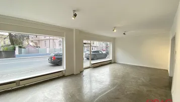 Geräumiger, leerer Gewerberaum mit großen Schaufenstern zur Straße hin und Betonboden.