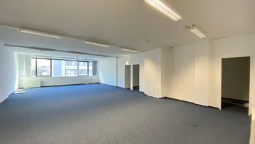 Großes, leeres Büro mit blauem Teppichboden und großen Fenstern, bereit zur Renovierung.