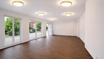 Großer, heller Raum mit großen Fenstern und Blick auf die Straße, ausgestattet mit modernem Laminatboden und Deckenleuchten.