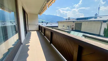 Geräumiger Balkon mit Fliesenboden, Markise und weitem Blick auf die umliegenden Berge und Dächer.