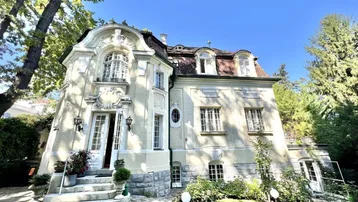 Elegante historische Villa mit aufwendiger Fassade und gepflegtem Vorgarten unter blauem Himmel.