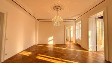 Helles Zimmer mit kunstvollem Parkettboden, hohen Decken und elegantem Kronleuchter, durchflutet von Sonnenlicht.