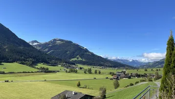 Weitläufiger Blick über grüne Felder und majestätische Berge unter strahlend blauem Himmel.