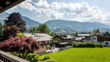Panoramablick vom Balkon auf die umliegende Berglandschaft und grüne Wiesen.