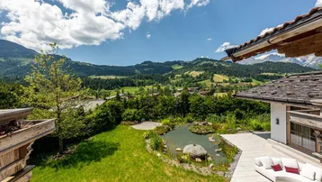 Idyllischer Gartenbereich mit Naturteich, Liegefläche und weitem Blick auf die Berge und grüne Landschaft.