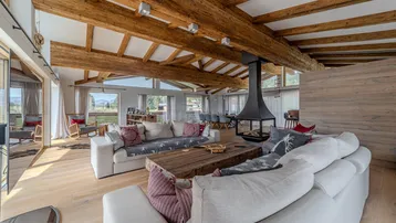 Geräumiges Wohnzimmer mit freiliegenden Holzbalken, modernem Kamin und bequemen Sofas.