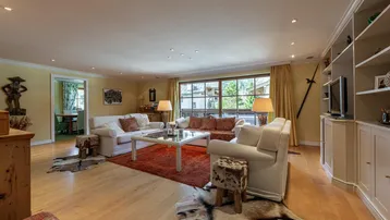 Geräumiges Wohnzimmer mit hellen Sofas, Holzboden und Blick ins Grüne durch große Fenster.
