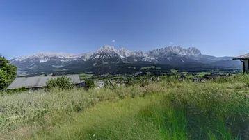 Panoramablick auf die majestätischen Berge und das Tal mit Häusern unter klarem blauem Himmel.