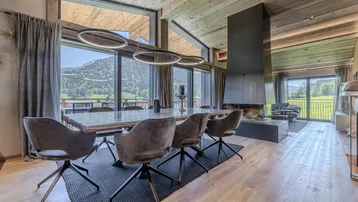 Moderner Essbereich mit großem Holztisch, bequemen Stühlen und beeindruckendem Bergblick durch Panoramafenster.