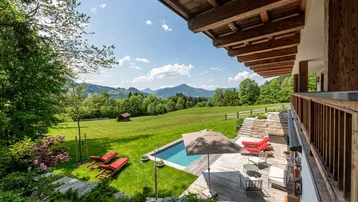Sonnige Terrasse mit Pool, Liegestühlen und weitem Blick auf die umliegende Berglandschaft.