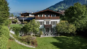 Großzügiges Anwesen mit Bergblick, umgeben von einem gepflegten Garten und Bäumen.