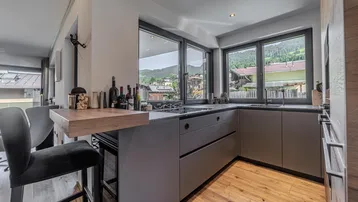 Moderne Küche mit grauen Schränken, Frühstücksbar und Bergblick durch große Fenster.