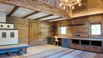 Geräumiges Wohnzimmer im alpinen Stil mit Holzbalken, Kachelofen und rustikalem Wagenrad-Kronleuchter.