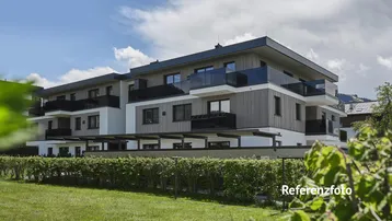 Modernes Mehrfamilienhaus mit Holzfassade und Balkonen, umgeben von Grünflächen unter blauem Himmel.