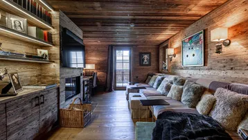 Gemütliches Wohnzimmer im alpinen Stil mit Holzwänden, bequemer Sitzbank und integrierten Regalen.