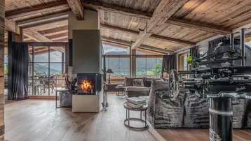 Geräumiges Wohnzimmer im alpinen Stil mit Kamin, Holzbalkendecke und Panoramablick auf die Berge.
