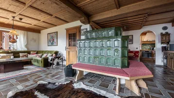 Geräumiges Wohnzimmer mit traditionellem Kachelofen, Holzbalkendecke und rustikalem Fliesenboden.