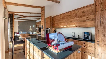 Moderne Holzküche mit Kochinsel, dunkler Arbeitsplatte und Blick in den Wohnbereich.