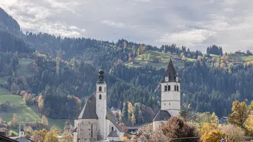 Malerischer Blick auf eine Stadt mit historischen Kirchen vor einer beeindruckenden Berglandschaft.