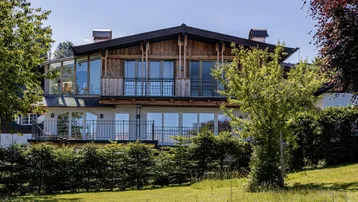 Großzügiges Wohnhaus mit Holzfassade, großen Fensterfronten und Balkonen in grüner Umgebung.