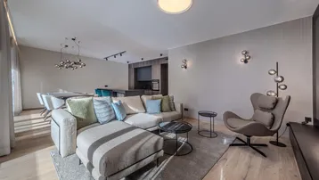 Moderner offener Wohn- und Essbereich mit beigem Sofa, Holzboden und integrierter Küche.