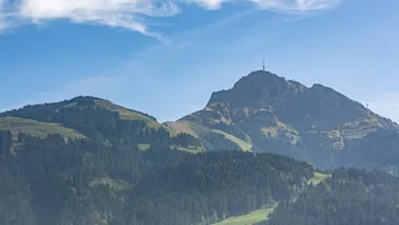 Malerischer Blick auf die umliegende Berglandschaft mit grünen Wäldern und blauem Himmel.