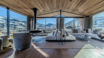 Großzügiges Wohnzimmer mit Holzbalkendecke, Panoramafenstern und freistehendem Kamin mit Bergblick.
