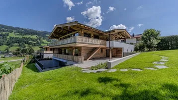 Modernes Holzhaus im Chalet-Stil mit großem Garten und Bergblick unter blauem Himmel.