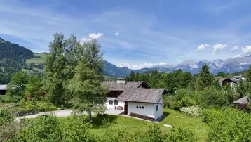 Idyllisches Einfamilienhaus in ländlicher Umgebung mit Bergblick unter blauem Himmel.