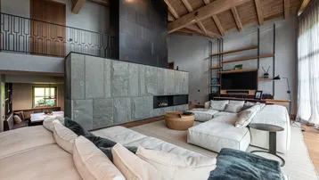 Geräumiges Wohnzimmer mit hohen Holzdecken, modernem Kamin und bequemen Sofas, offen zu einer Galerie.