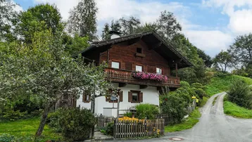 Traditionelles Holzhaus im Alpenstil mit blumengeschmücktem Balkon, umgeben von viel Grün.