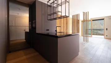 Moderne offene Küche mit dunkler Arbeitsplatte, Holzwandverkleidung und Zugang zu einem Außenbereich.