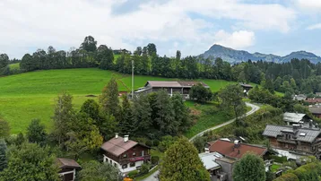 Weitläufige Ansicht der ländlichen Umgebung mit Häusern, grünen Hügeln und fernen Berggipfeln.