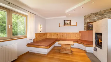 Gemütlicher Wohnbereich mit Kamin, Holzboden und eingebauter Sitzbank am Fenster mit Grünblick.