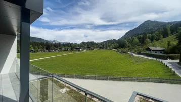 Blick vom modernen Balkon über grüne Wiesen und die umliegende Berglandschaft.