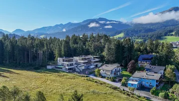 Luftaufnahme des modernen Gebäudekomplexes eingebettet in grüne Landschaft mit Bergen.